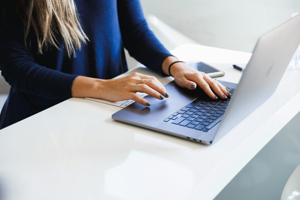 Dłonie kobiety piszące na laptopie przy białym biurku