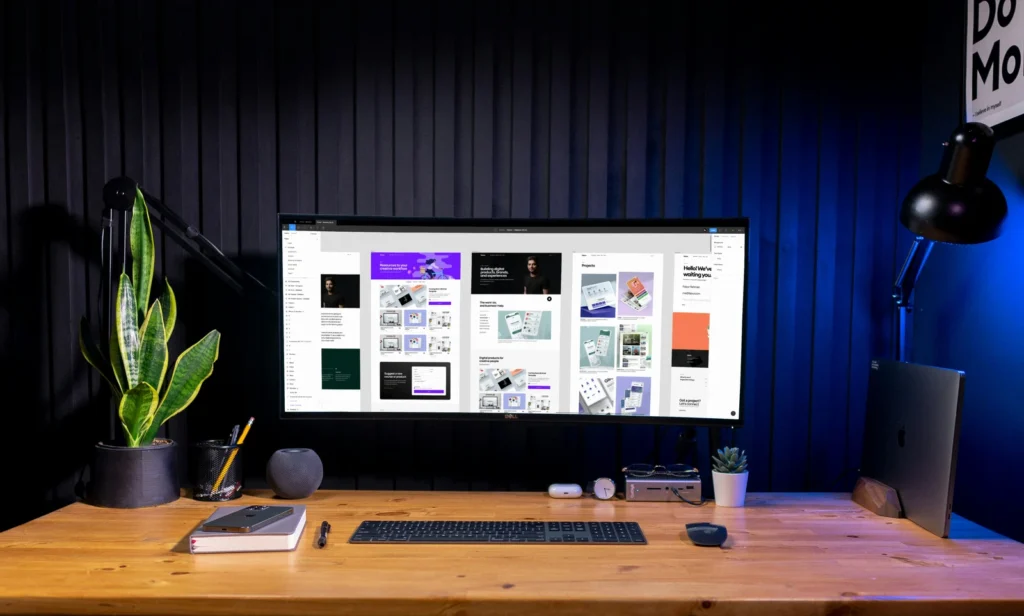 Biurko z dużym monitorem i rośliną w ciemnym pokoju