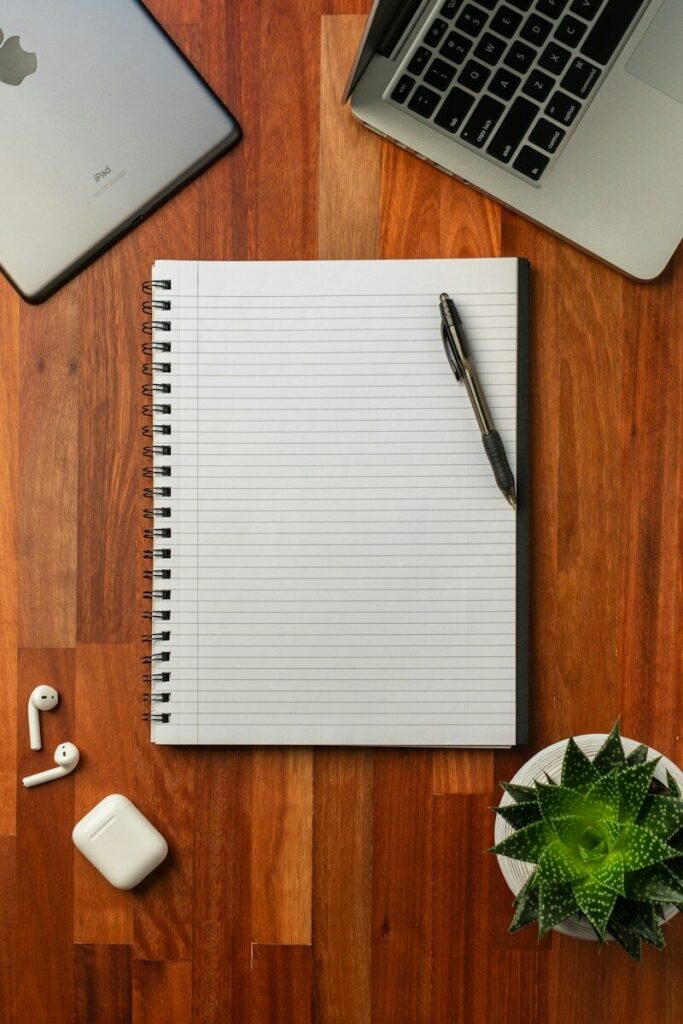 Otwarty notes z długopisem obok laptopa na drewnianym biurku